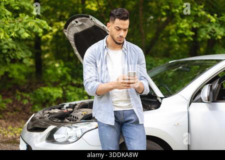 Sad arab man looking for auto service, using smartphone Stock Photo