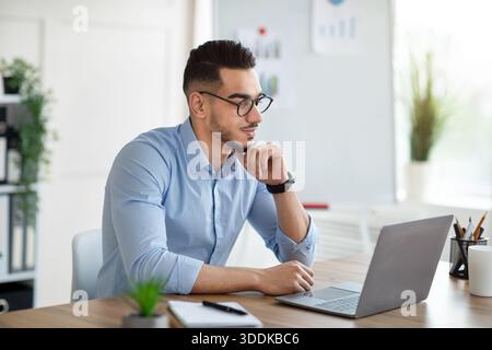 Positive Arab businessman using laptop pc at workplace, speaking to colleagues on webcam Stock Photo