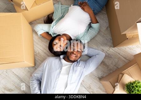 Loving african american couple lying among cardboard boxes on floor of their new apartment, top view Stock Photo