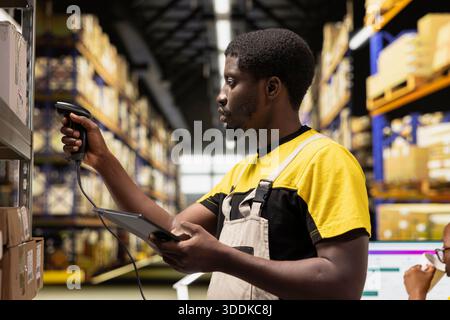 African american e-commerce worker scanning shipping labels numbers, registering awb and shipment details for the inventory records. Young man handling pallets distribution operations. Stock Photo