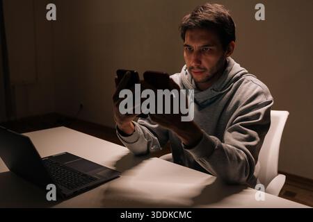 Young man holding two smartphones, focused on comparing apps and messages, multitasking between screens for work or personal digital communication and Stock Photo