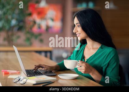 Smiling middle-eastern lady freelancer enjoying her job, cafe interior Stock Photo