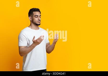 Religious young arab man praying on yellow background, copy space Stock Photo