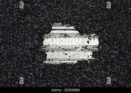 Close-up of cracked asphalt with exposed white metal underneath. Stock Photo