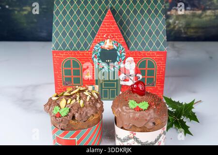 Two panettone cakes covered in melted chocolate in front of a Christmas house-shaped box. Stock Photo