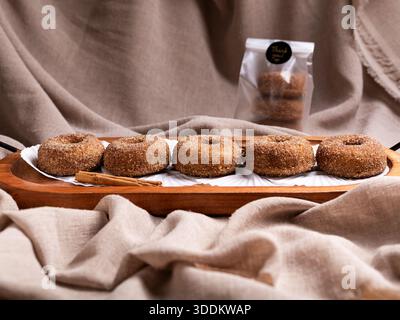 Rustic cinnamon donuts placed on a wooden tray against a background of soft linen fabric and a bag of donuts. Citron donuts. Stock Photo