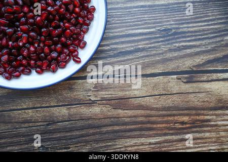 Fresh pomegranate seeds in glass bowl on textured wooden table Stock Photo