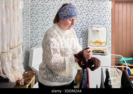 Middle aged woman hanging washed laundry on drying rack in bathroom. Stock Photo