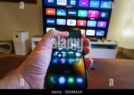 Streaming platforms icon home entertainment smartphone television remote control living room. Hand holding modern smartphone displaying streaming serv Stock Photo