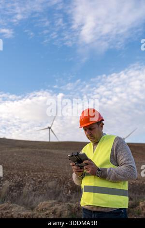 Engineer operating remote drone at wind farm, performing inspection and monitoring renewable energy infrastructure Stock Photo