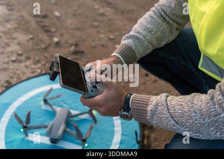 Experienced technician using a remote control and smartphone to operate a surveying drone, getting ready for an aerial examination Stock Photo