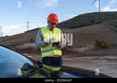 Engineer wearing safety vest and hard hat using drone controller for pre flight setup, preparing for industrial inspection Stock Photo