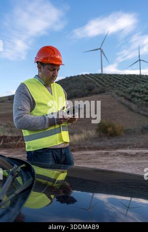 Engineer wearing a hard hat and high visibility vest controlling a drone preparing for inspection of wind turbines in wind farm Stock Photo