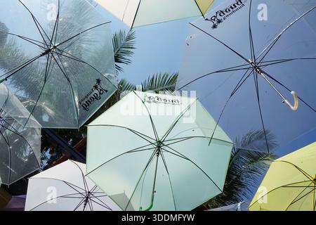 Penang, Malaysia, December 5, 2025: Colorful umbrellas suspended overhead form a playful outdoor art against blue sky and palm trees at Kg Penaga. Stock Photo