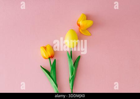Spring composition with yellow Easter egg and yellow tulip on pastel pink background. Creative Easter concept. Unique festive holiday layout. Stock Photo
