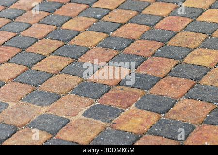 A close-up view of a patterned walkway made from orange, yellow, and gray interlocking paver tiles. The warm tones and geometric layout convey durabil Stock Photo