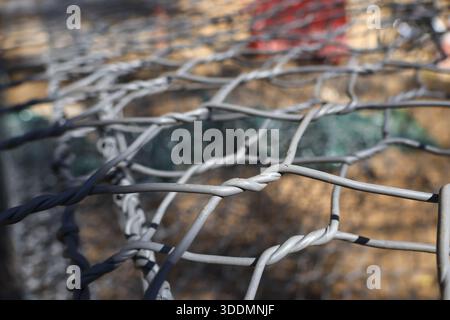 Close up twisted steel wire mesh cage gabion basket with blurry stones background showing strong metallic texture and pattern in industrial constructi Stock Photo