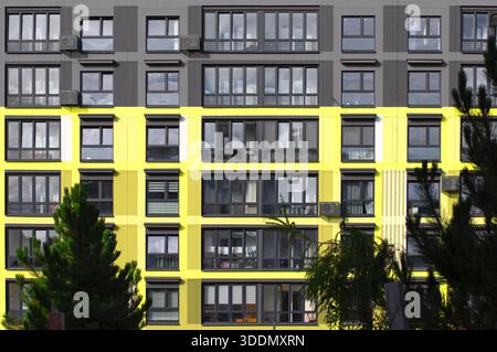 Modern residential building facade with bright yellow accents, large glass windows, and a repetitive geometric pattern, creating a striking urban arch Stock Photo
