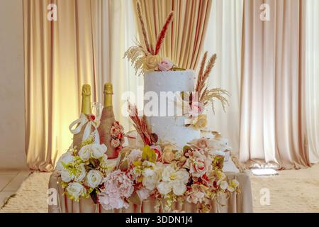 Elegant white wedding cake with champagne bottles and floral decorations Stock Photo