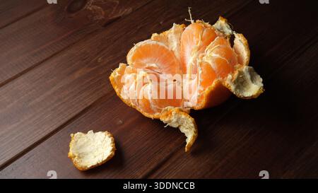 Bright orange mandarin sits on a rustic wooden table, segments visible and inviting. Stock Photo