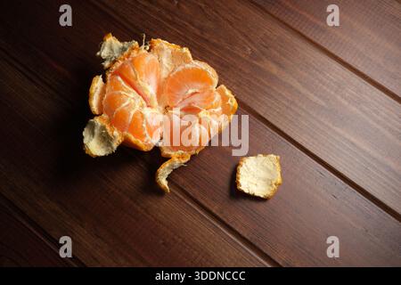 A vibrant mandarin sits open on a rustic wooden surface, ready to enjoy. Stock Photo