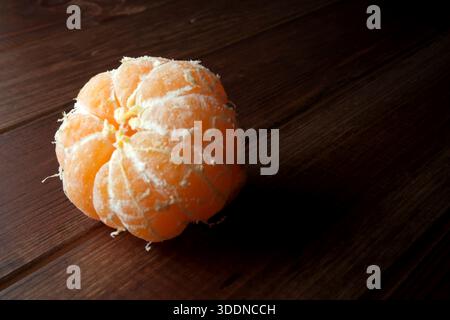 A peeled orange fruit sits alone on a dark, textured wood table, inviting and fresh. Stock Photo