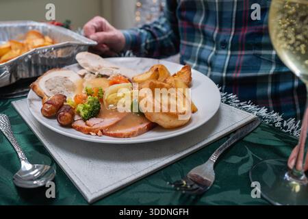 Christmas dinner served on a white plate. The dish includes pigs in blankets, vegetables, turkey and gammon. There is also a Yorkshire pudding and roa Stock Photo