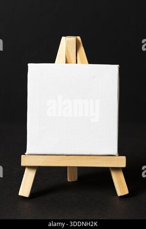 Blank mini white canvas on wooden easel on dark background. template mockup Stock Photo