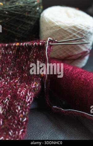 Cozy knitted socks on needles with yarn balls. Mix of red, green and white yarn on knitting needles. Knitting process of wool socks. Knitting hobby. Stock Photo
