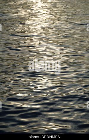 Water surface abstract composition of various circular waves and flowing shapes, illuminated by golden hues Stock Photo
