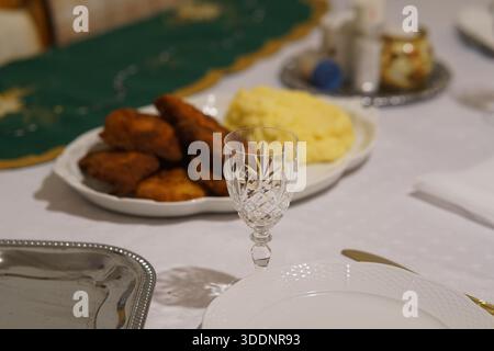 Elegant dinner table set with breaded cutlets, mashed potatoes, and crystal glassware for a festive family meal.Budapest,Hungary Stock Photo