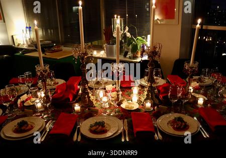 Christmas dinner table, table cloth, candle sticks with ornaments, red napkins, first course pre-plated, waiting for dinner guests to festive meal. Stock Photo
