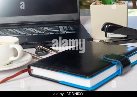 Notebook Laptop Coffee Cup On Desk, Pen, Glasses, Stapler And Succulent Plant Nearby, Leather Planner With Elastic Band And Blue Bookmark, Black Lapto Stock Photo