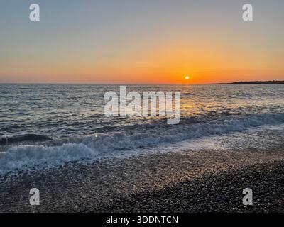 Sunset over calm sea with gentle waves and pebble beach Stock Photo