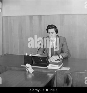 Slaviansk, Ukrainian SSR, Soviet Union, 1980s. An authentic archival working portrait of Comrade Novikov, director of the AIZ Armature and Insulator Plant, sitting at his desk in a wood-paneled office. The man is dressed in a suit and tie, focused on reading documents and handling business papers. The desk features a calendar stand, books and a decorative ceramic shoe. This vintage black and white photograph captures the daily routine of a Soviet industrial leader and the stability of the peaceful Donbas region during the USSR era. Stock Photo