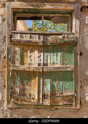 Old wooden window frame and crumbling shutters on an aged stone wall Stock Photo