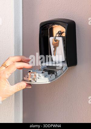 Hand opening a wall-mounted key safe containing house keys, providing secure access Stock Photo