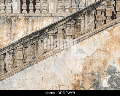 Old stone balustrade on an ancient outdoor staircase with weathered walls and peeling plaster Stock Photo