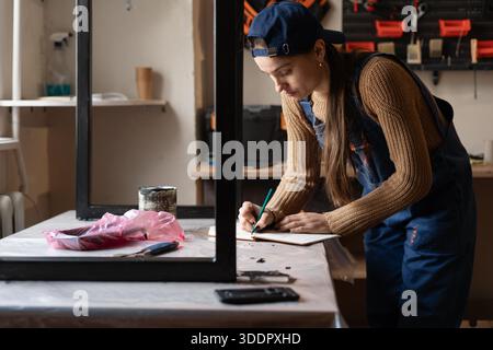 Female handyman writing or checking repair checklist in her repair workshop Stock Photo