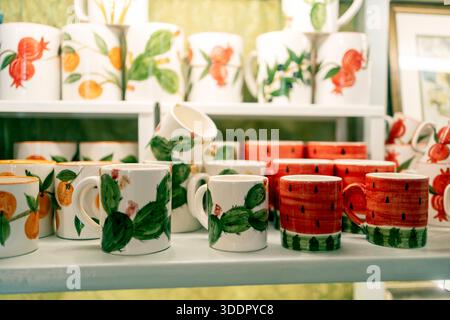 Shelf display of handmade ceramic mugs painted with fruit and cactus patterns in a gift shop. Stock Photo