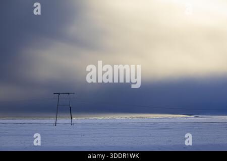 View of stark, snow-covered plains stretch under a dramatic sky, where dark, brooding clouds meet a soft, ethereal glow on horizon, Golden Circle, Ice Stock Photo