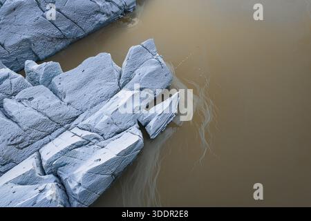 Aerial view of jagged blue icebergs drift in ochre waters, a stark contrast of frozen giants against the muted tones of the glacial lagoon, southern I Stock Photo