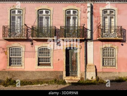 Weathered pink facade with wrought iron balconies and arched windows, Lisbon, Portugal Stock Photo
