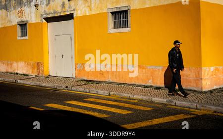 Moody street photography, solitary man by yellow wall and zebra crossing, Alcântara, Lisbon, Portugal Stock Photo
