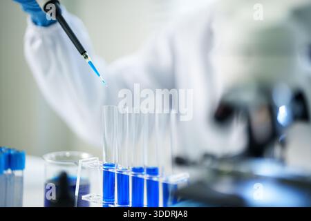 Scientist conducting precise laboratory analysis using micropipette on blue liquid samples in test tubes for medical innovation. Focused research. Stock Photo