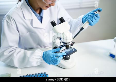 Asian adult researcher meticulously performs scientific experiment in modern laboratory setting using advanced optical microscope and micropipette dev Stock Photo