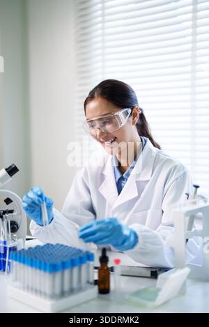 Adult Asian female professional performs scientific investigation in a modern lab. She explores new findings with precision and expertise. Stock Photo