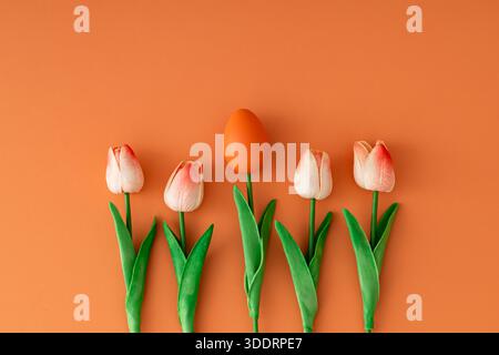 Spring surreal composition with orange Easter egg and tulips on orange background with copy space. Creative Easter concept. Stock Photo