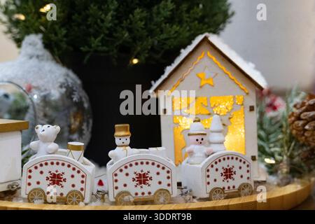 A cozy holiday scene featuring a white and gold miniature train, snowman and bear figurines, pine branches, and warm Christmas lights Stock Photo