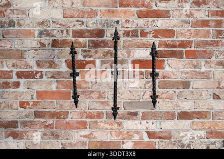 Brick wall featuring three vertically aligned black wrought iron decorative elements. The composition reflects traditional European architecture with Stock Photo